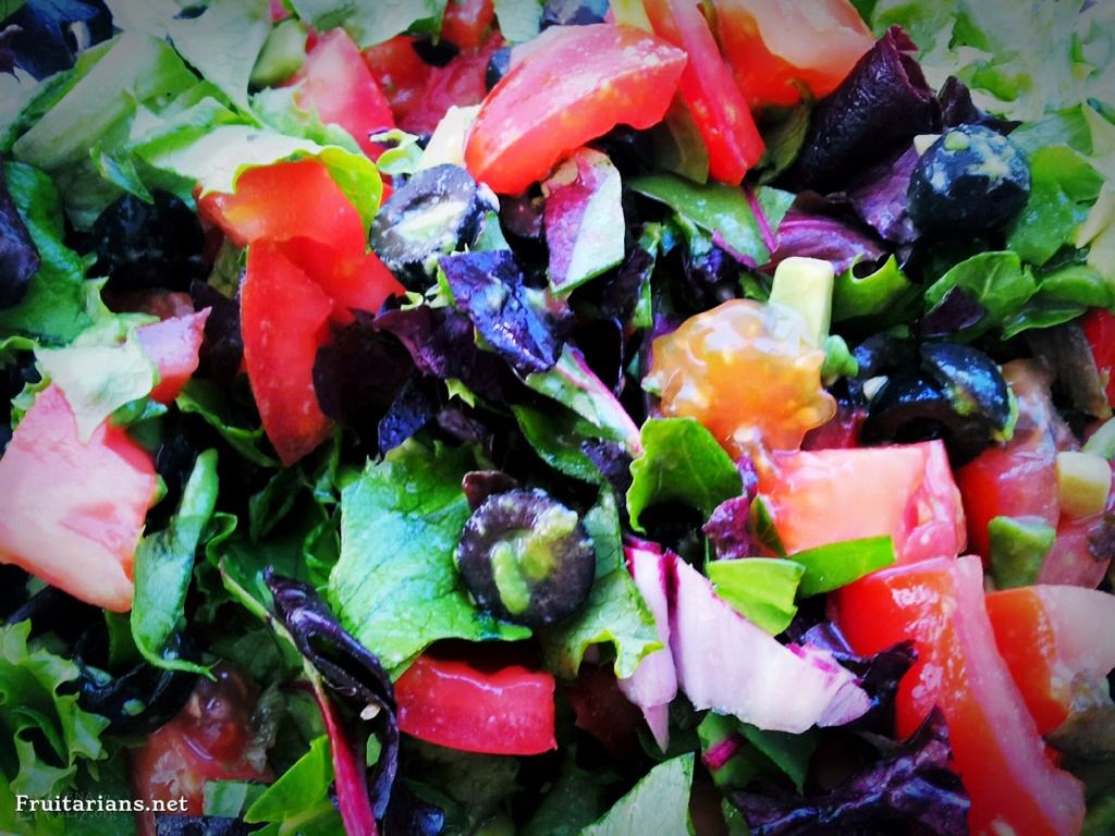 Adding mixed leafy greens to a fruit salad. 